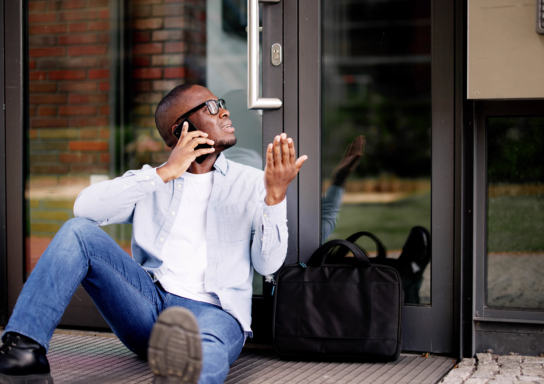 Man sitting locked up infront of a door with phone in hand.